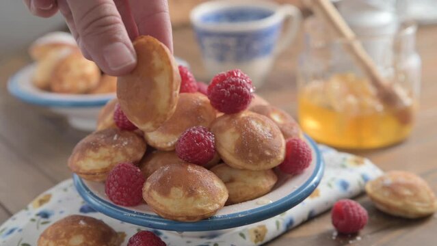 Close-up of golden Dutch Poffertjes with syrup and berries. Delicious traditional mini pancakes on a plate. the , honey pours on mini pancakes in a white plate with a blue pattern