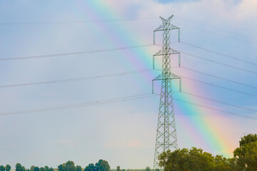 A metal tower of a high-voltage line of electrotransfers in the background of a stormy sky after a rain with a multicolored rainbow. Natural atmospheric phenomena and modern technologies. Weather.