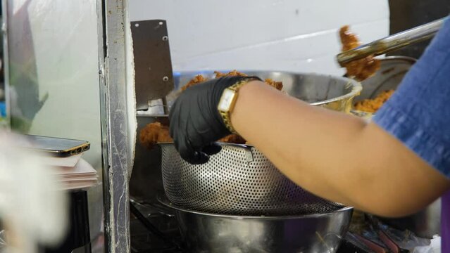 Vendor putting Gai Tod fried chicken in a bowl or strainer. Traditional Thai street food concept