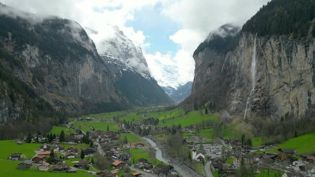 Fly over Sweeping view of a lush green Alpine valley under a dramatic cloudy sky, with rugged mountain cliffs. Lauterbrunnen, Switzerland, Slow Motion, 4K RAW. 