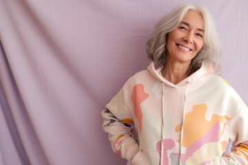 A playful senior woman laughs heartily in a kidcore-inspired, multicolor hoodie, her silver hair and joyful demeanor challenging age stereotypes.