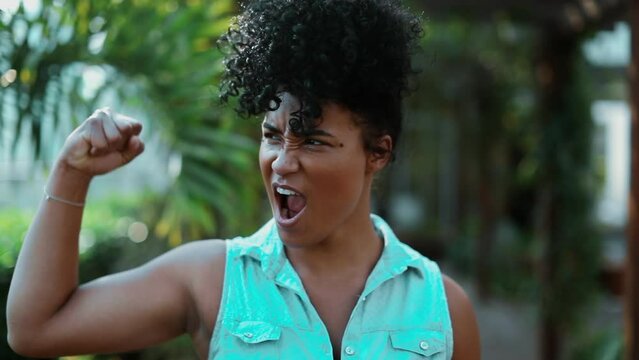 One young confident black woman making strength gesture showing muscle with arm while walking forward, flexing arm and smiling