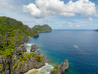 Fototapeta premium Coastline wiith limestone rocks and boat over the blue sea. Matinloc Island. El Nido, Philippines.