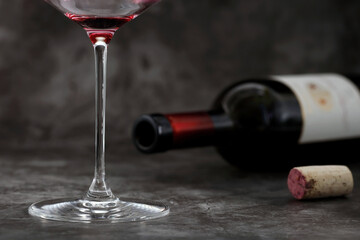 Empty glass of wine in front of lying wine bottle with cork on dark gray background, concept of alcoholism or excessive alcohol consumption, close-up of last sip of wine