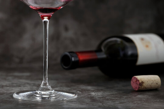 Empty glass of wine in front of lying wine bottle with cork on dark gray background, concept of alcoholism or excessive alcohol consumption, close-up of last sip of wine