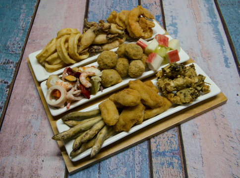 Mediterranean antipasti. Top view of a plate with seafood salad and dishes such as fried squid rings, fried whitebait, fish balls and croquettes, with a rustic wooden background. 