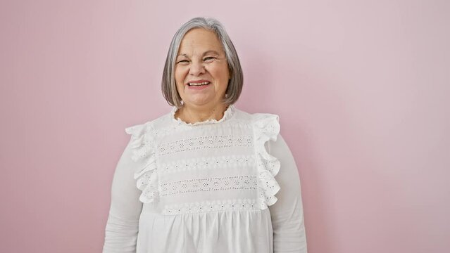 Joyous grey-haired, middle age woman in shirt, standing confidently with toothy smile, exuding positive energy over isolated pink background