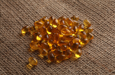 Fish oil capsules on burlap background close up