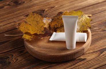 White cream tubes on a wooden plate with autumn leaves. Beauty mockup