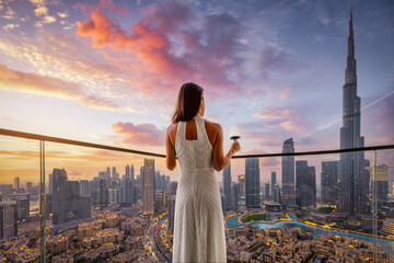 A elegant woman in a white evening dress enjoys the beautiful sunset view behind the modern skyline of Downtown Dubai, UAE