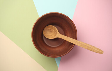 Clay bowl with wooden spoon on pastel background. Top view