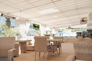 Wicker furniture tables in the open air are waiting for visitors. The interior of the restaurant in the open air. Empty tables of street cafe.