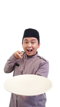 Asian Muslim man holding empty dinning plate and drinking glass. Indonesian muslim man holding dinning plate and pointing it. Ramadhan concept. Happy asian Muslim man looking at the camera. 