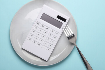 Plate with calculator and fork on a blue background. Reset evening, count calories