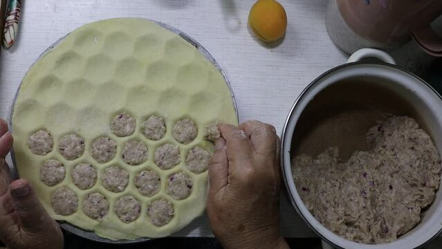 Grandma cooks dumplings using a dumpling mold and a pot of meat