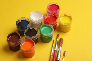 Jars of gouache paint with brushes on a yellow background