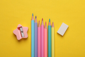 Sharpener with eraser and colored pencils on yellow background