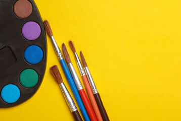 Watercolor paint palette with brushes on a yellow background