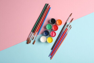Set of gouache paint in bottles and brushes on a blue-pink background