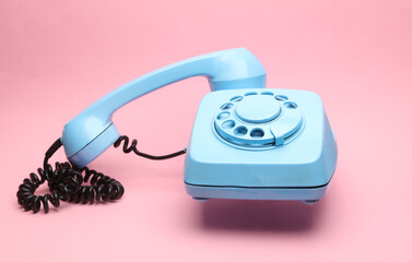 Blue retro rotary phone floating on pink background