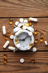 Different types of pills in white plastic bottles with alarm clock on a wooden table. Top view