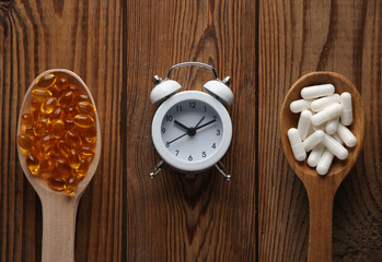 Pills in spoons and alarm clock on a wooden table. Treatment of insomnia