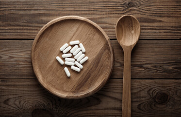 White pills with wooden plate and spoon on table.  Top view