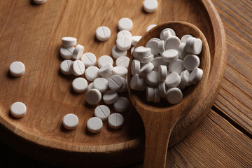 White pills with wooden plate and spoon on table.  Top view