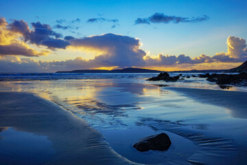 Les nuages se reflètent sur le sable mouillé à marée basse, une scène captivante sur une plage...