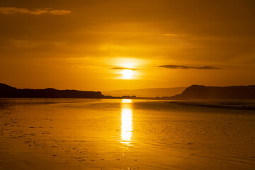Le soleil se reflète sur le sable mouillé, lui conférant des teintes dorées et orangées, une vision enchanteresse sur la Presqu'île de Crozon en Bretagne. - obrazy, fototapety, plakaty