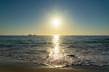 Soleil éclatant en fin de journée sur une plage bretonne, sous un ciel bleu reflétant dans la mer et sur le sable. - obrazy, fototapety, plakaty