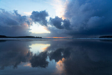 Au crépuscule, les nuages se reflètent délicatement sur le sable mouillé d'une plage de la Presqu'île de Crozon en Bretagne, créant une scène paisible et poétique.
