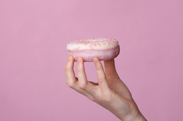 Glazed donut in a female hand on pink background