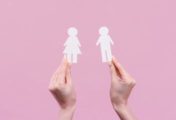 Woman's hand holds a paper cut woman and man on pink background