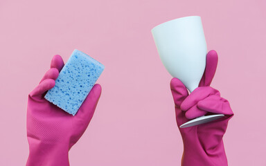 Hands in purple rubber cleaning gloves holding sponge and glass on a pink background.