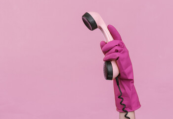 Hand in purple rubber cleaning glove holding retro phone tube on a pink background
