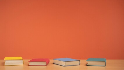 Old books with colored covers on a wooden table on a bright orange background.