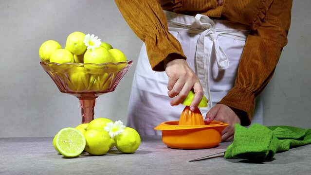 Female hand squeezes fresh lemon juice on orange plastic squeezer 