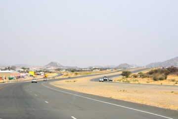 Fototapeta premium Car view of a winding asphalt road in the desert in perspective with cars driving ahead under a blue sky