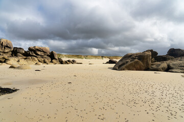 Plage bretonne, gigantesques rochers émergeant du sable, sous un ciel menaçant.