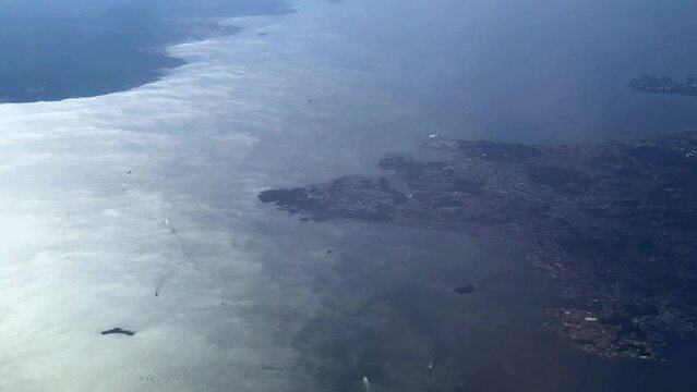 Coastline with cloud shadows over the sea, hint of urban area visible, aerial view