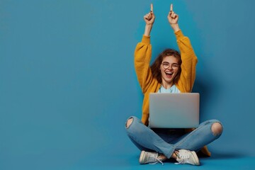 A woman is sitting on the floor with a laptop in front of her. She is smiling and holding up her hands in the air. Concept of excitement and enthusiasm