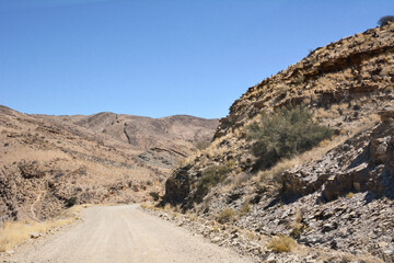 A dirt road in perspective between stone hills in the desert under a blue sky