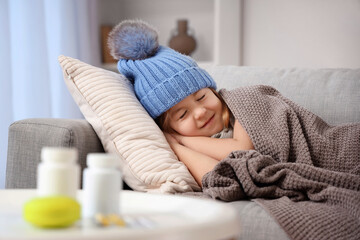 Sick little girl in hat sleeping on sofa at home