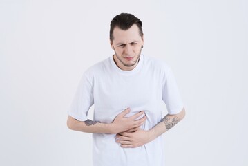 Attractive Caucasian young man with tattoos in casual clothes touching his stomach and suffering...