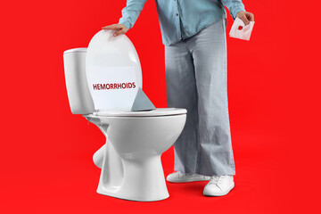 Mature woman with bloody paper and thumbtack on toilet bowl against red background. Hemorrhoids...