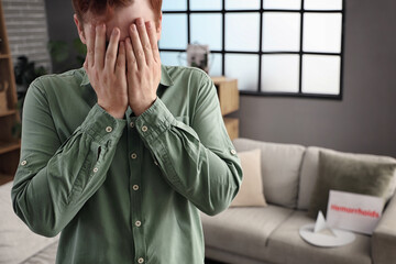 Young man with hemorrhoids and paper thumbtack on sofa at home, closeup