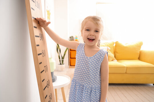 Cute little girl measuring height near wooden stadiometer at home