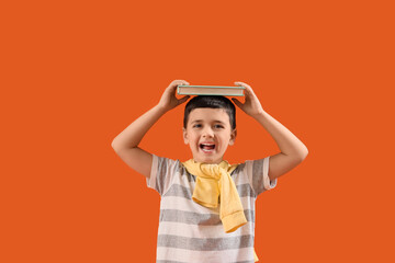 Cute little boy with book measuring height on orange background