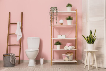 Interior of stylish bathroom with ceramic toilet bowl near pink wall